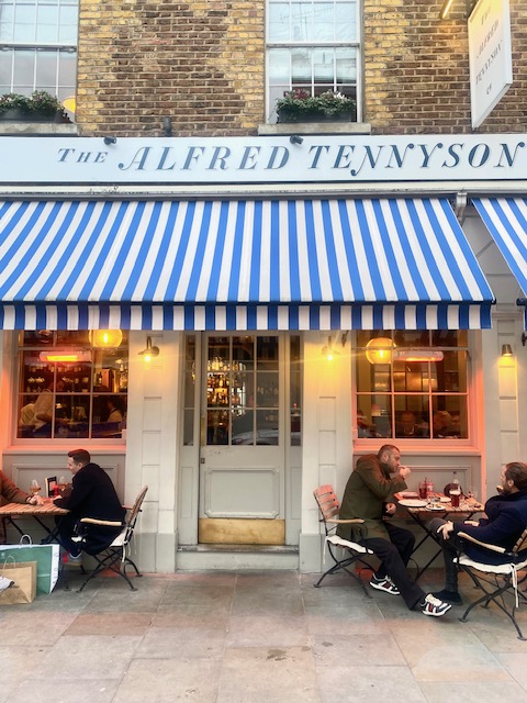 The outside of the Alfred Tennyson pub in Belgravia. Showing blue and white awnings and tables on the pavement.